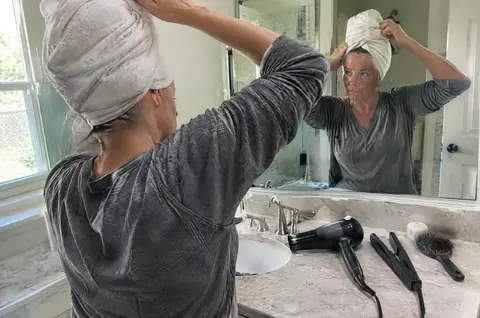 Woman twisting wet hair in a towel next to a hot blow dryer and flat iron